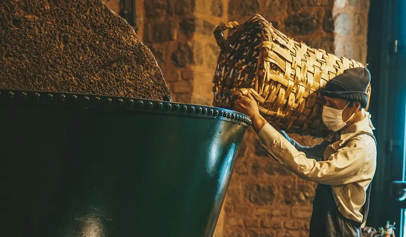 Person carrying a woven basket over their shoulder in a dimly lit room with a brick wall.